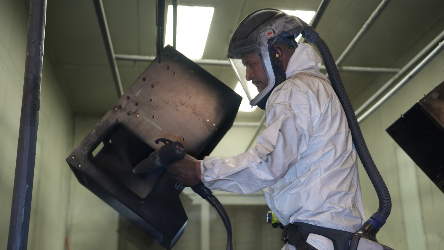 A worker in ppe setting up a part to be painted